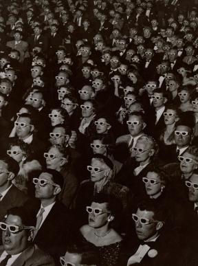A theater full of audience members wearing 3-D glasses and watching a movie. 
